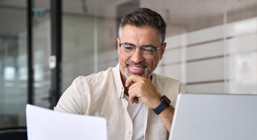 Mann im Büro vor seinem Laptop und Papier